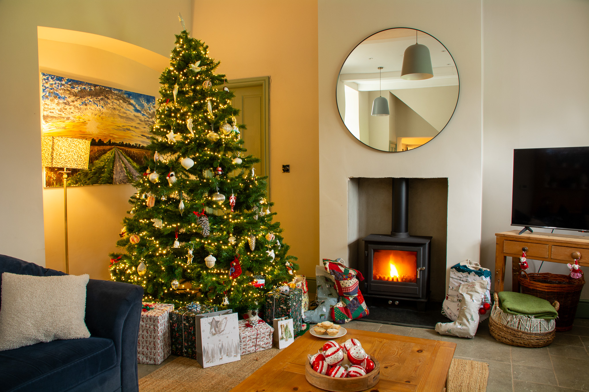 Cosy Christmas cottage living room with decorated tree, roaring log burner, and presents.
