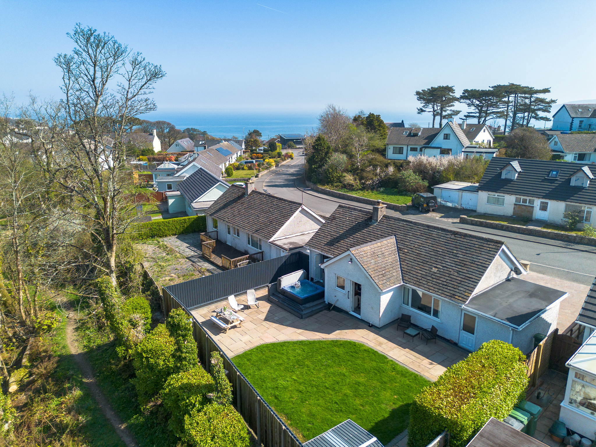 Aerial shot above the garden and hot tub at 80 Breeze Hill holiday cottage in Benllech, Anglesey, overlooking the sea