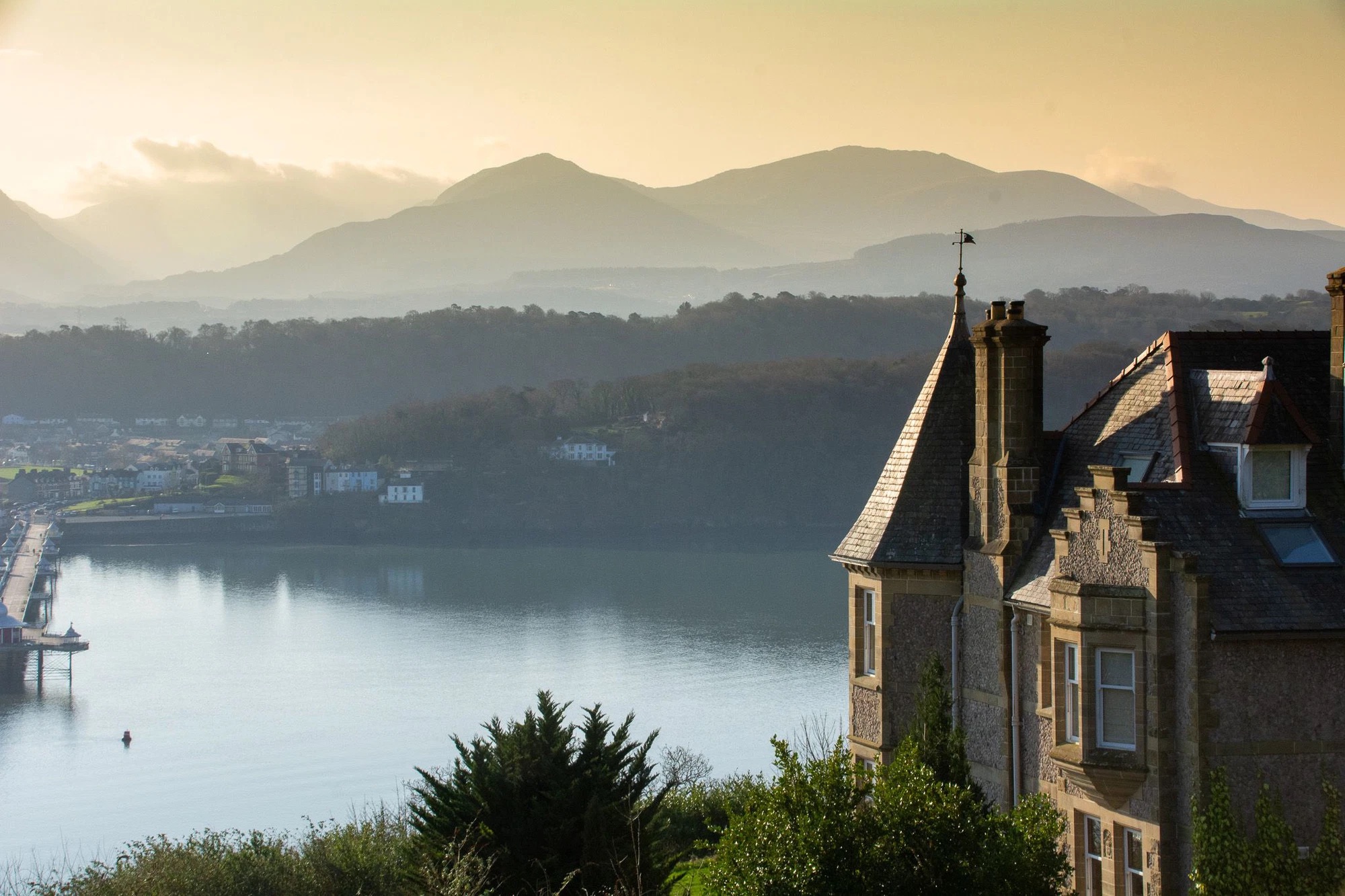 Aerial shot above Nyth Y Fran penthouse in Bryn Mel Manor overlooking the Menai Strait, Bangor Pier and Snowdonia mountain range in Menai Bridge, near Beaumaris, Anglesey