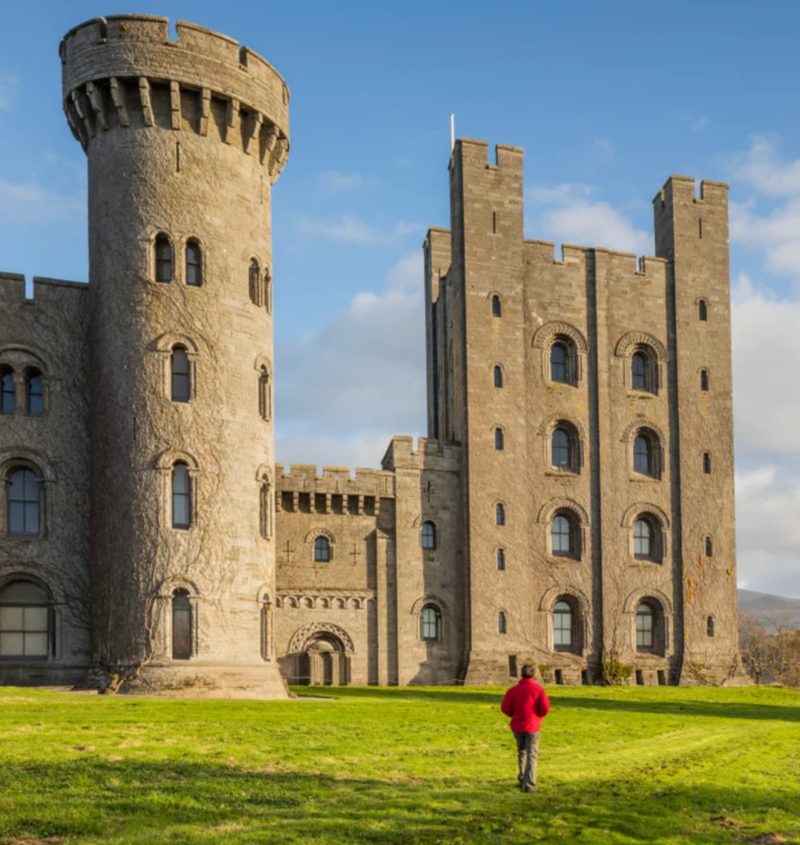 Walker approaching Penrhyn Castle Neo-Norman architecture with North Wales hills in the background