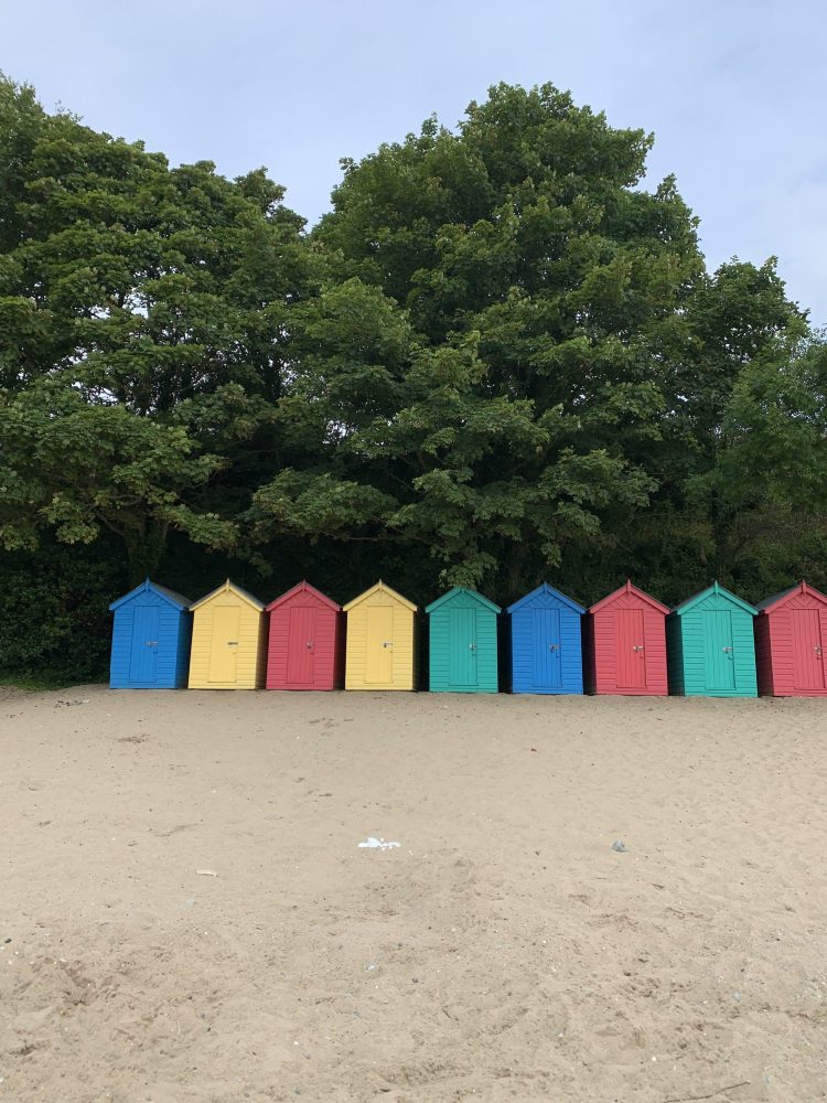 Llanbedrog Beach on the Llyn Peninsula, North Wales, with its iconic colourful beach huts backed by a wooded hillside