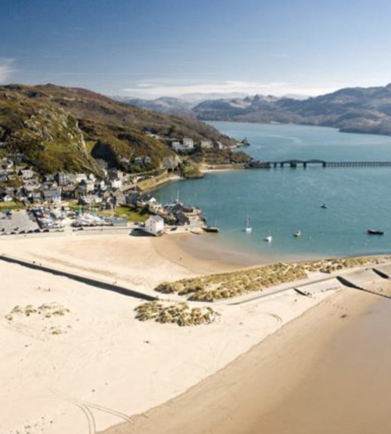 Aerial view of Barmouth Beach in southern Snowdonia, a wide sandy stretch with a classic seaside resort backdrop and mountain views over Cardigan Bay