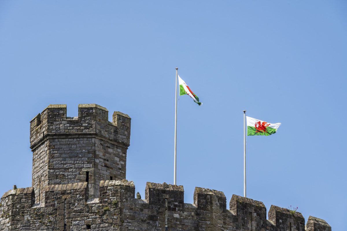 An image of Caernarfon castle turrets with Welsh flags against a blue sky