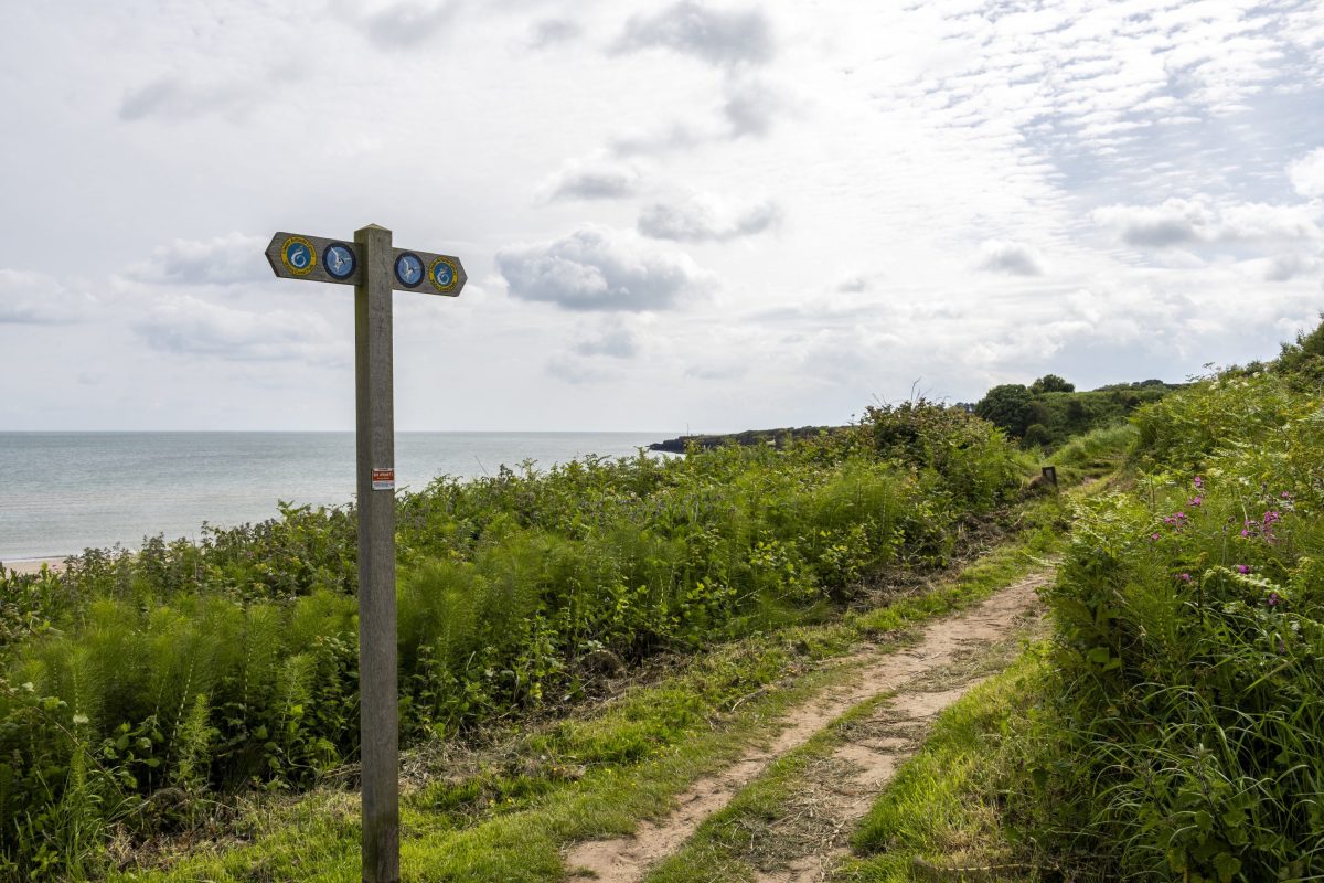 An image of a wooden welsh coastal path sign with the sea in the background 