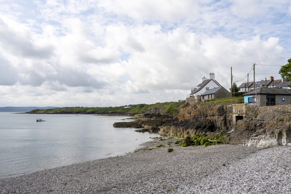 A view from Moelfre Bay of the pebble beach and green headland