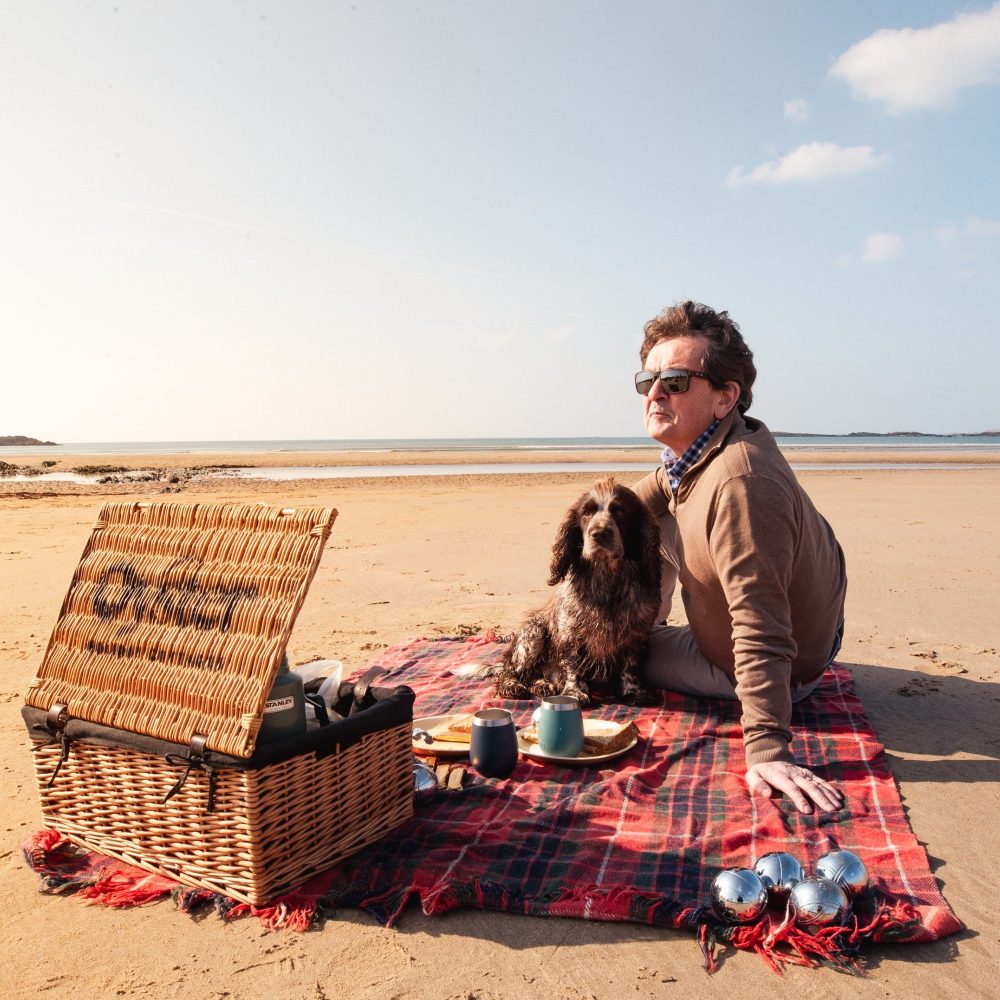 A man pets his dog while having a picnic on Silver Bay (Traeth Llydan), Rhoscolyn, a dog friendly beach on Anglesey
