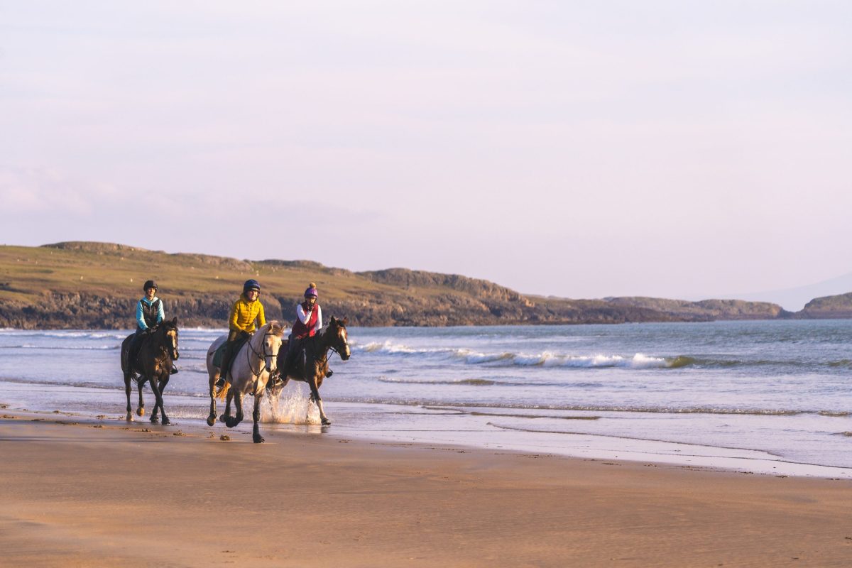 Three people riding horses along Aberffraw beach shoreline 