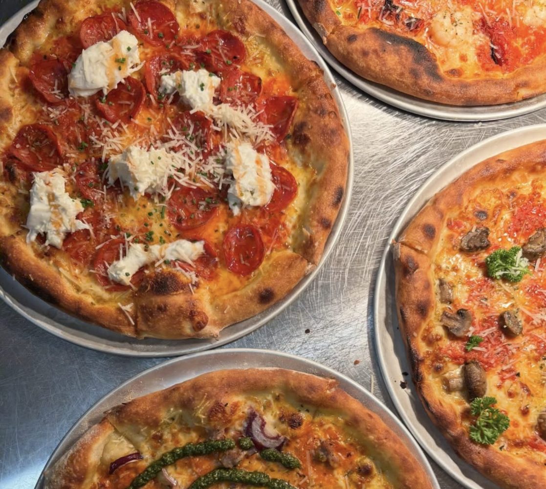 A flat lay shot of four different pizzas atop a stainless steel worktop from Pwllheli's Pitsa & Co restaurant
