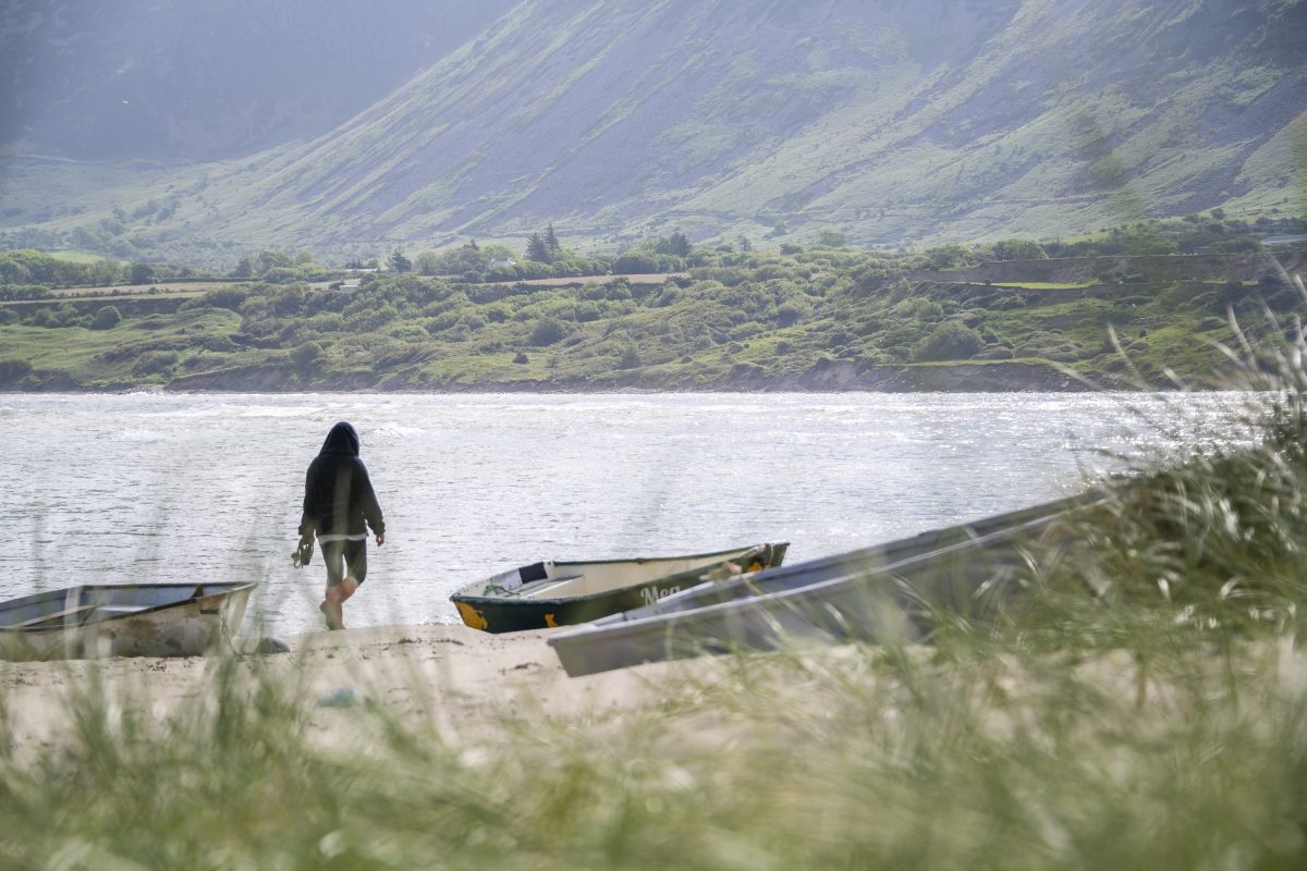 A lone person walking along the beach between wooden fishing boats in North Wales