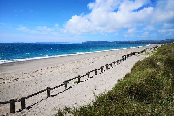 Pwllheli's main beach in the sunshine, with wooden fence line and Llanbedrog headland in the distance