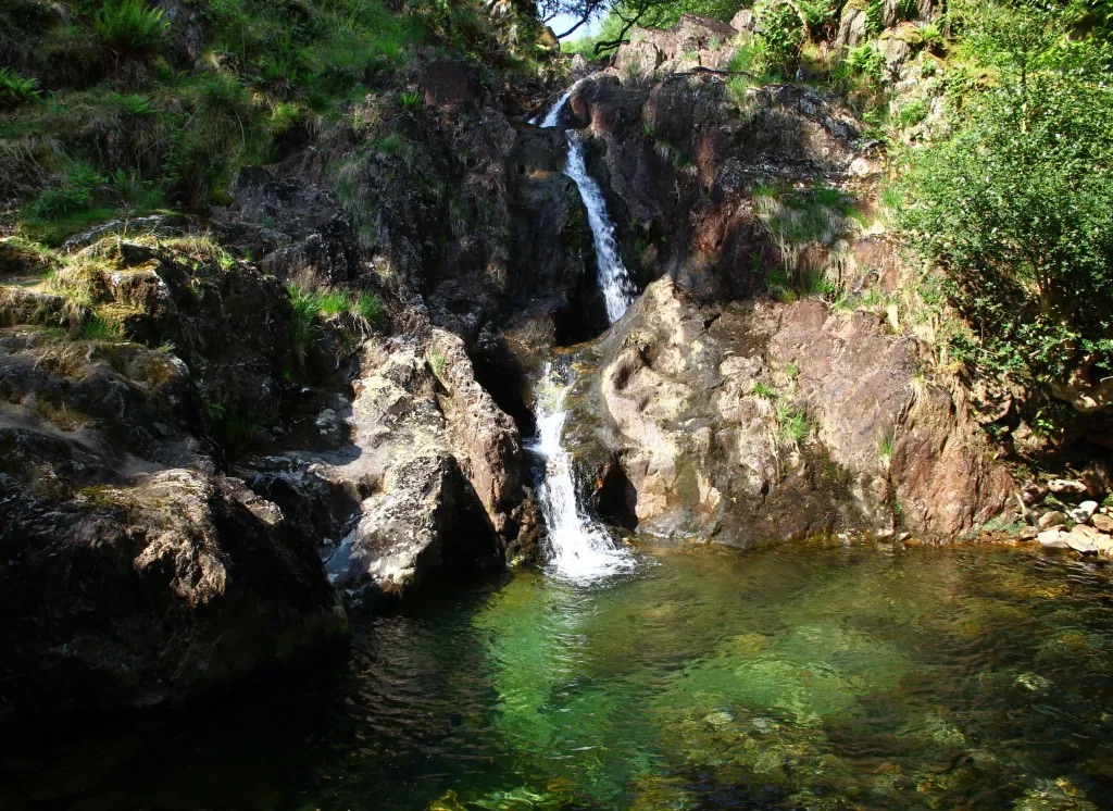 the emerald green waters of merlin's pool and the small waterfall behind it, snowdonia 